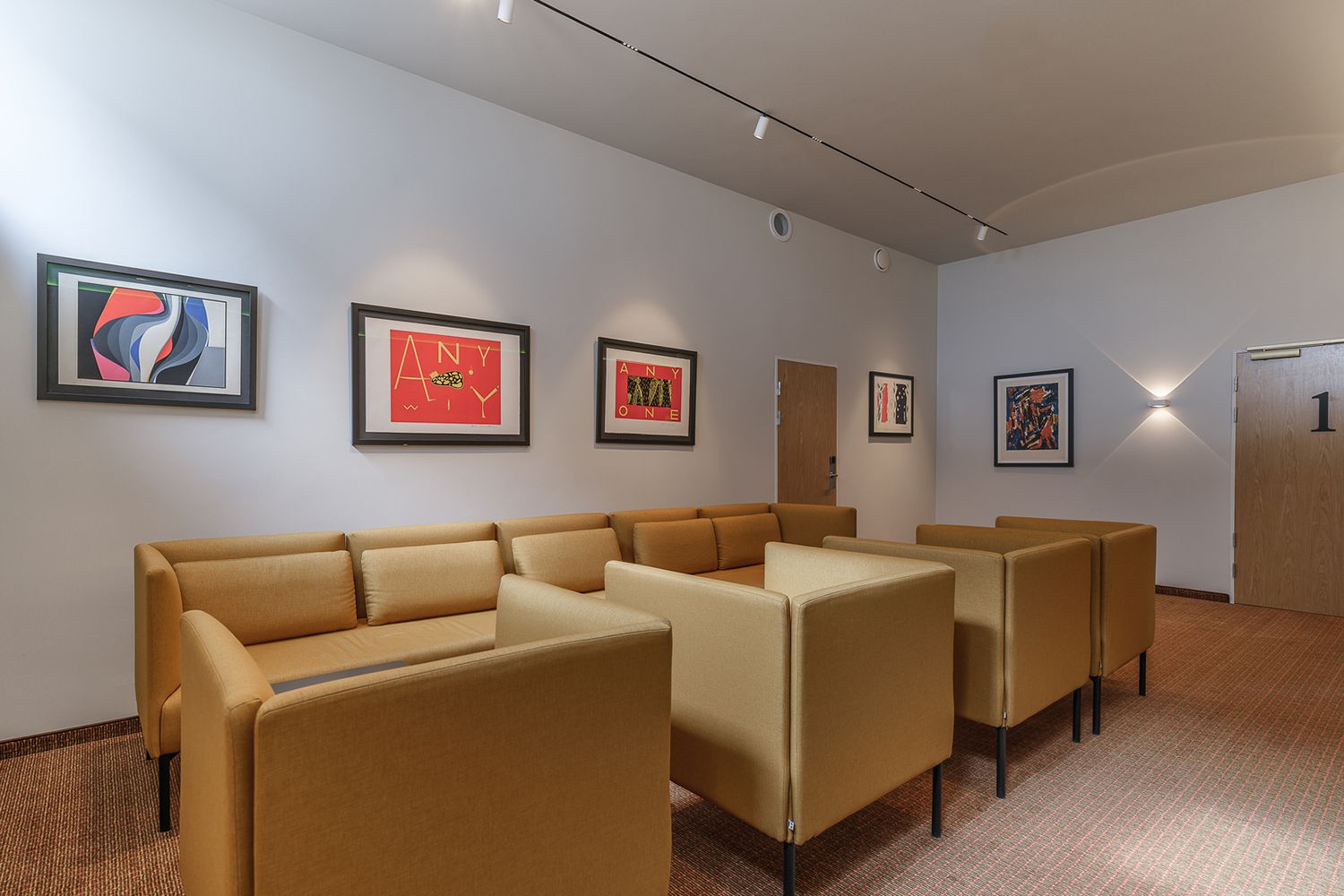 Rom ved gule sofaer og innfelt belysningssystem i taket som belyser kunst på veggen.