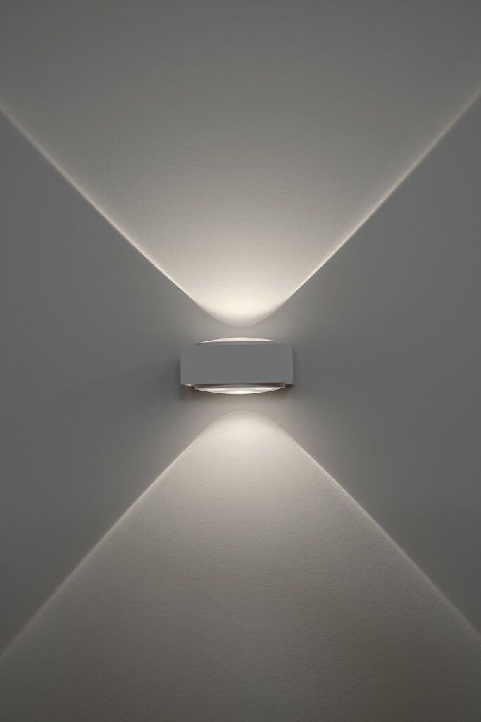 Hvit vegglampe på en hvit vegg som lyser opp og ned.