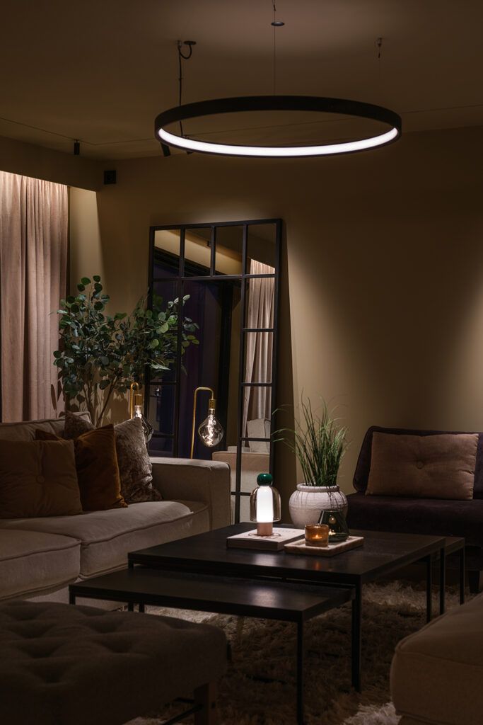 Slepelys langs en gardin i en stue og lys i lampe over stuebord.