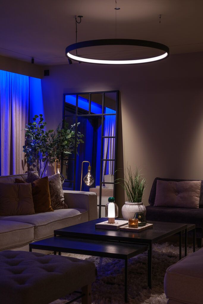 Rund pendel over spisebord og blålig slepelys langs gardiner.