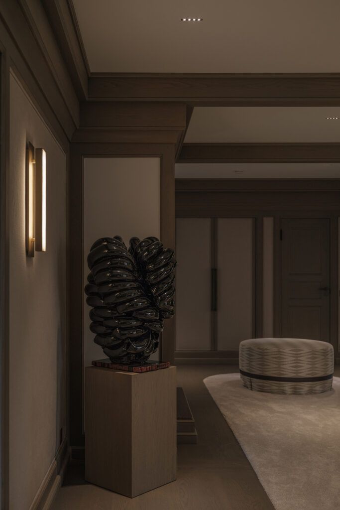 Vegglampe og spotter i tak som belyser kunst som står på et podie.