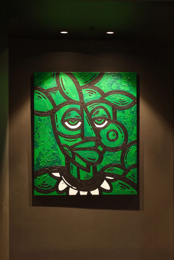 Grønt bilde på en vegg belyst av spotter i taket.