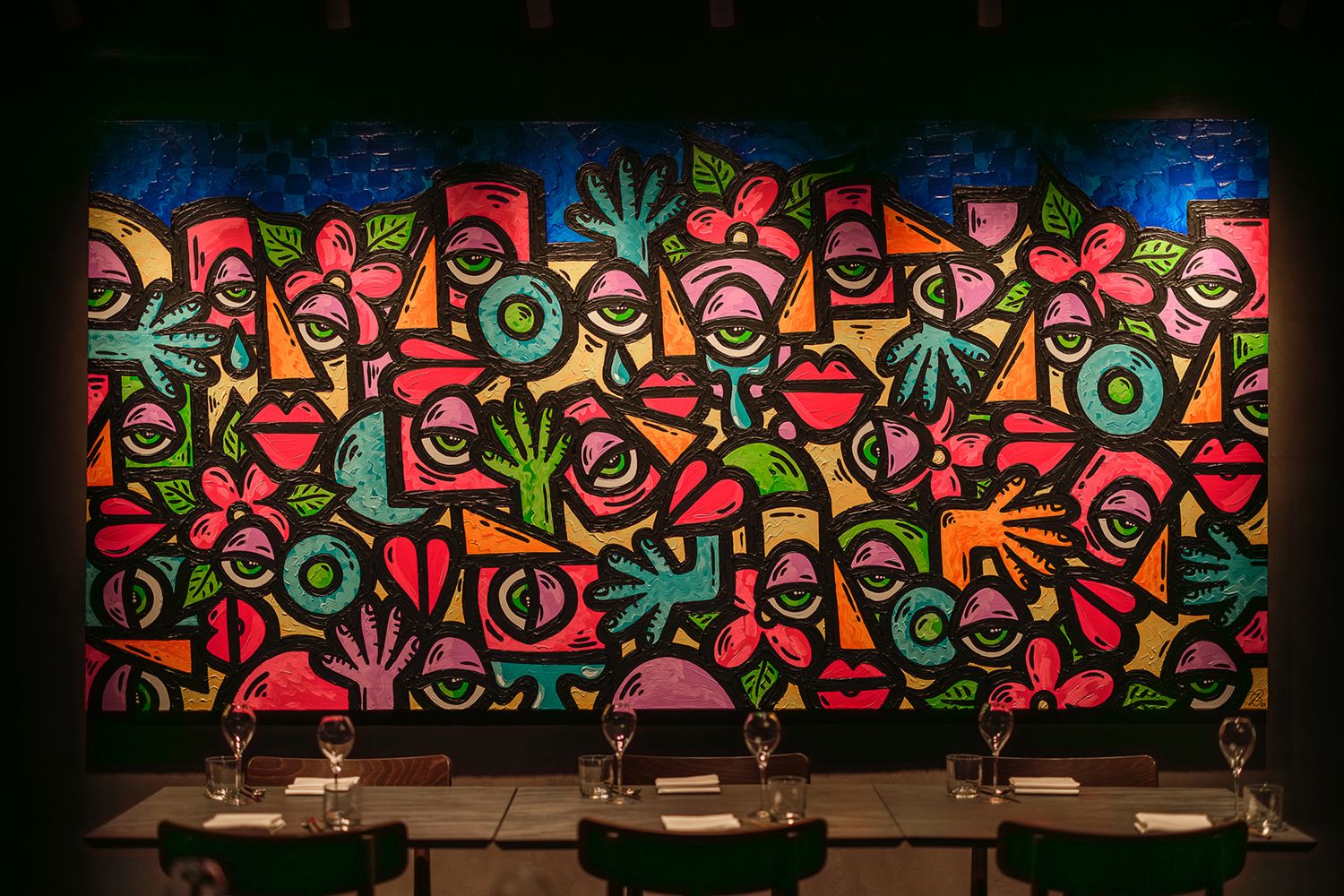 Stort fargerikt bilde på veggen belyst av spotter i taket.